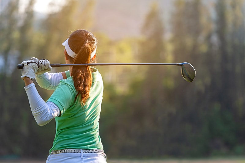 Sport Healthy. Asian sporty woman golf player doing golf swing tee off on the green sunset evening time, she presumably does exercise. Healthy and Lifestyle Concept.