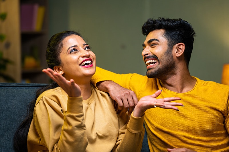 Happy young couple on sofa talking closely at home during weekend night - concept of conversation, affectionate and feelings or emotions.