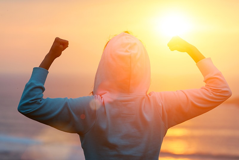 Back view of strong motivated woman celebrating workout goals towards the sun. Morning healthy training success.