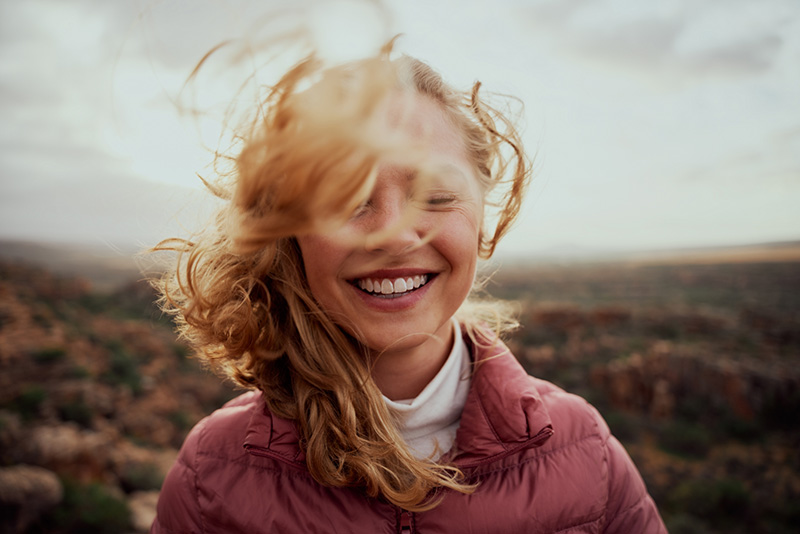 Smiling woman with windblown hair standing in a field.